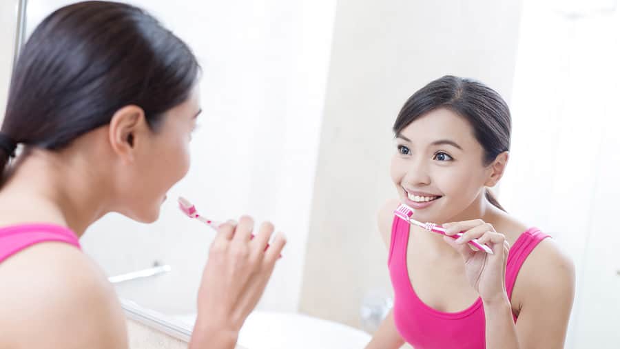 一位笑得燦爛的女性在對著鏡子刷牙