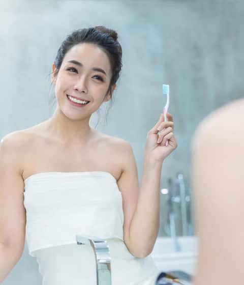 Portrait of beautiful young asian woman brushing teeth in front of bathroom mirror